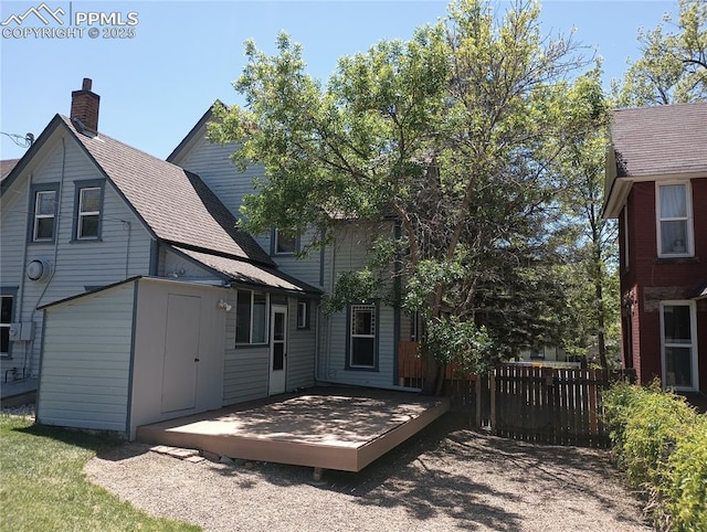 rear view of property with a wooden deck, roof with shingles, a storage unit, fence, and an outdoor structure