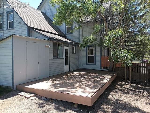 rear view of house featuring roof with shingles, fence, and a deck