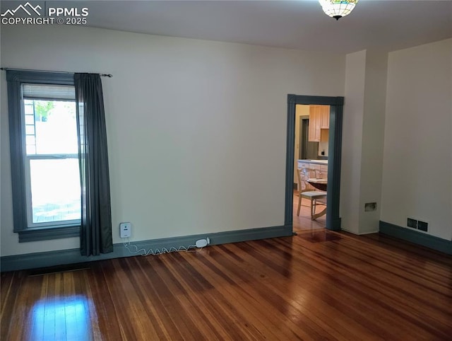 unfurnished room with visible vents, baseboards, and hardwood / wood-style flooring