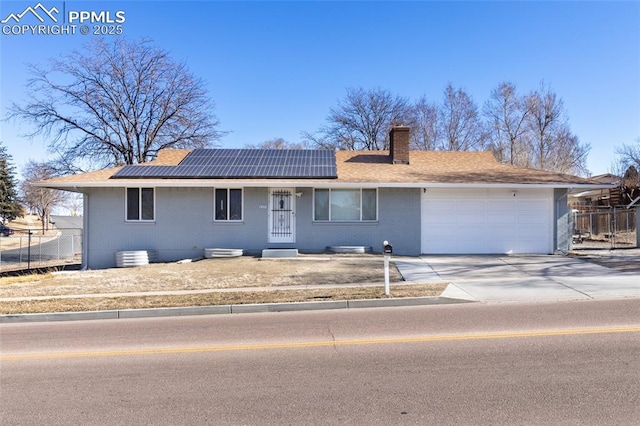 single story home featuring driveway, roof mounted solar panels, fence, and a chimney