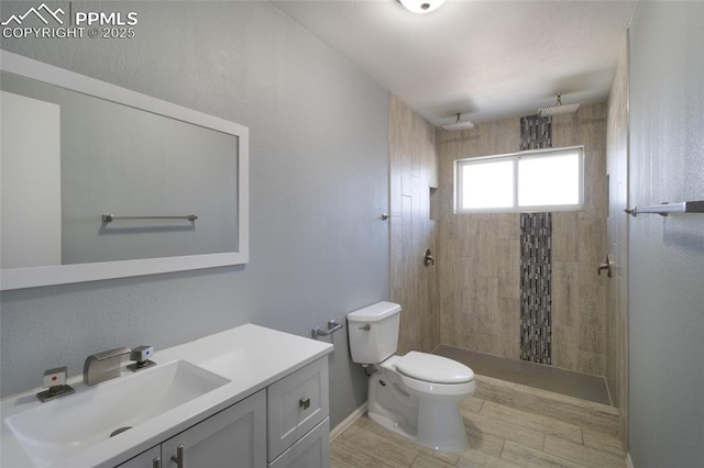 full bath featuring baseboards, a tile shower, vanity, and toilet