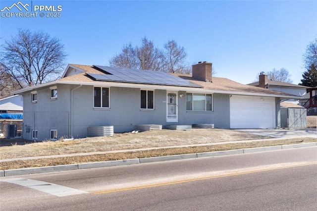 single story home with brick siding, a chimney, an attached garage, and roof mounted solar panels