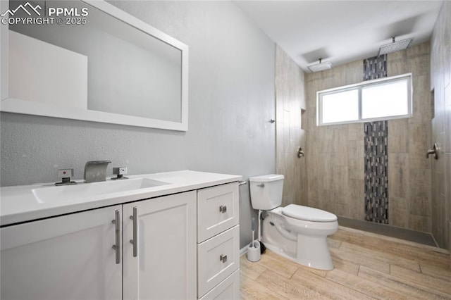 full bath featuring a tile shower, wood finished floors, vanity, and toilet