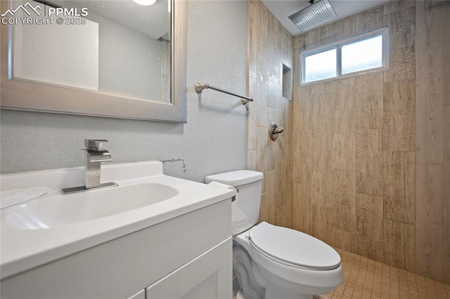 full bathroom with tiled shower, a textured wall, vanity, and toilet