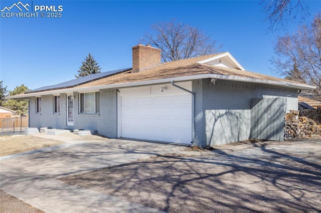 exterior space with a garage, solar panels, concrete driveway, a chimney, and brick siding