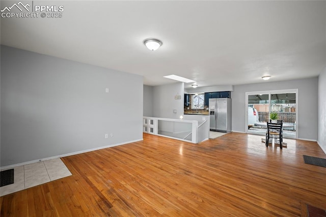 unfurnished living room with a skylight, visible vents, baseboards, and light wood-style floors