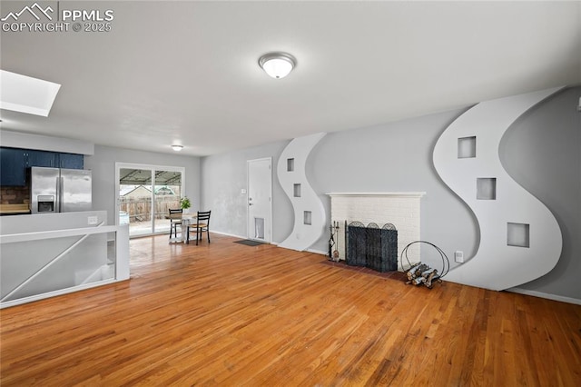 living area with a skylight, light wood-style flooring, and a brick fireplace