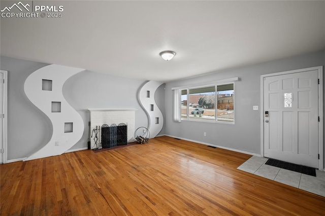 unfurnished living room with a brick fireplace, wood finished floors, visible vents, and baseboards