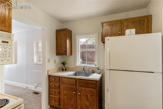 kitchen with white appliances, visible vents, brown cabinetry, and a sink