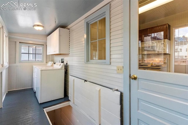 clothes washing area featuring a wealth of natural light, cabinet space, wood walls, and separate washer and dryer