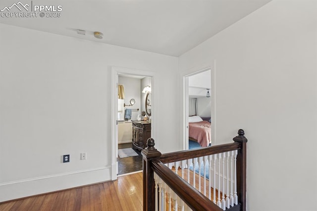 hall featuring light wood finished floors, baseboards, and an upstairs landing