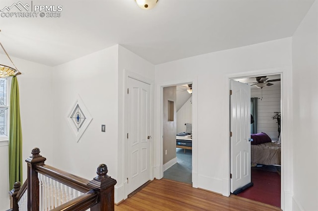 hallway featuring baseboards, wood finished floors, and an upstairs landing