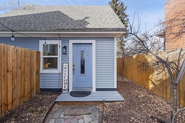 view of exterior entry with roof with shingles and fence