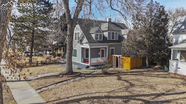 view of front of property with covered porch, a shingled roof, a chimney, and fence