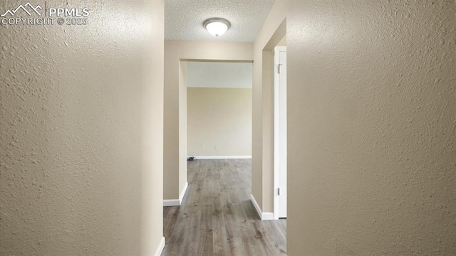 corridor featuring baseboards, a textured ceiling, wood finished floors, and a textured wall