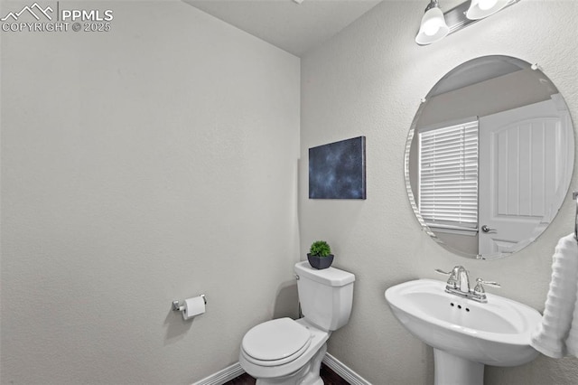 half bathroom with a sink, toilet, and baseboards