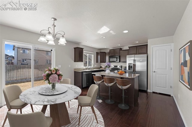 kitchen with dark brown cabinetry, baseboards, dark wood finished floors, a kitchen island, and appliances with stainless steel finishes