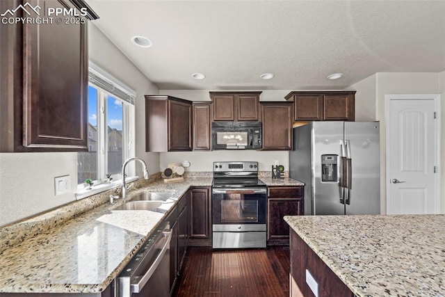 kitchen with dark wood finished floors, stainless steel appliances, a sink, dark brown cabinetry, and light stone countertops