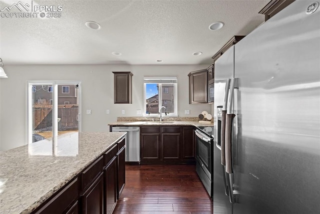 kitchen with dark wood-style floors, stainless steel appliances, a sink, dark brown cabinets, and light stone countertops