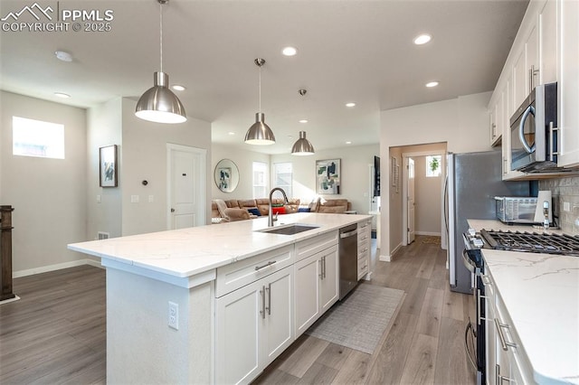 kitchen featuring white cabinets, decorative backsplash, open floor plan, stainless steel appliances, and a sink