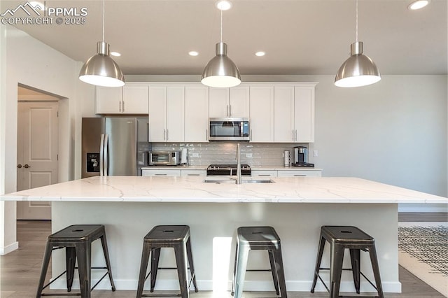 kitchen featuring white cabinets, decorative backsplash, an island with sink, stainless steel appliances, and a kitchen bar