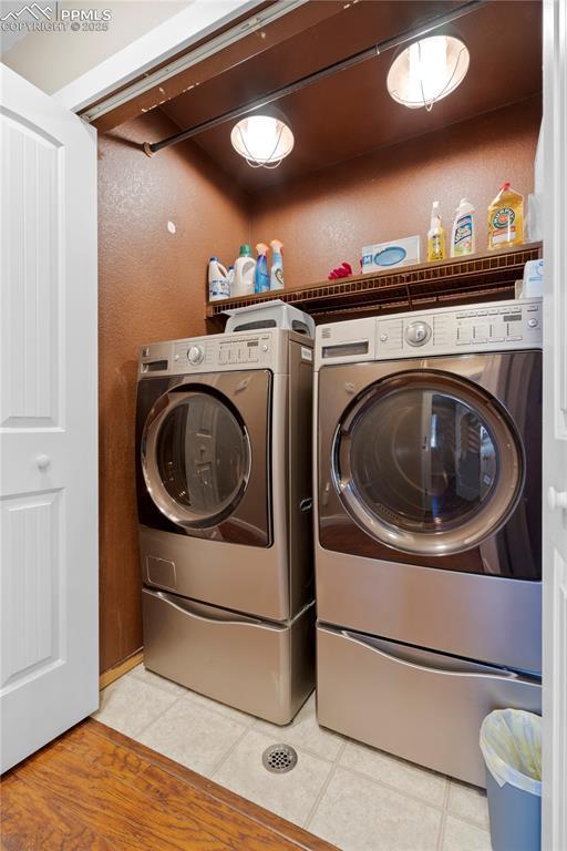 laundry room with laundry area, light tile patterned floors, a textured wall, and independent washer and dryer