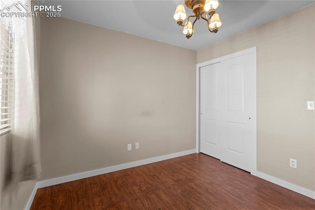 unfurnished bedroom featuring baseboards, a closet, wood finished floors, and a notable chandelier