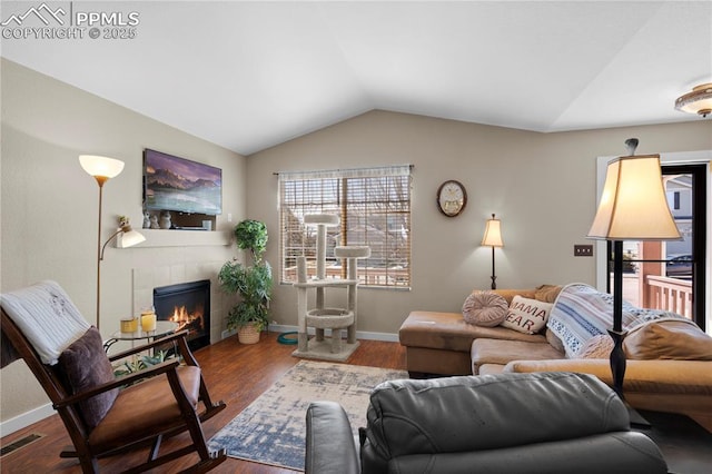 living room featuring lofted ceiling, wood finished floors, visible vents, a wealth of natural light, and a tiled fireplace