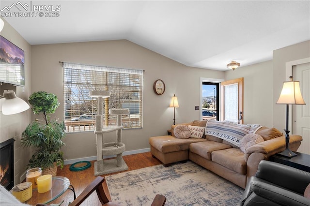 living area featuring a glass covered fireplace, vaulted ceiling, baseboards, and wood finished floors