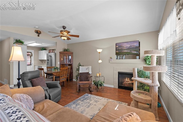 living room with lofted ceiling, a tiled fireplace, wood finished floors, and baseboards