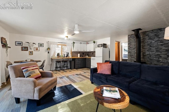 living area featuring a wood stove, light wood-style floors, and ceiling fan