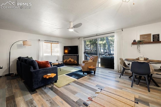 living area with ceiling fan, a textured ceiling, and wood finished floors