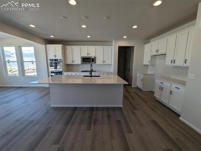 kitchen with dark wood finished floors, appliances with stainless steel finishes, a sink, and a kitchen island with sink