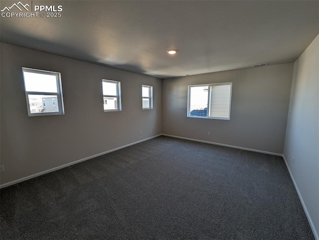 empty room with dark carpet, visible vents, and baseboards