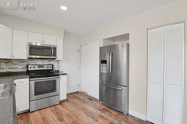 kitchen with tasteful backsplash, white cabinets, dark countertops, wood finished floors, and stainless steel appliances