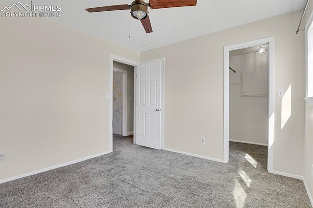 unfurnished bedroom with carpet, a closet, a spacious closet, a textured ceiling, and baseboards