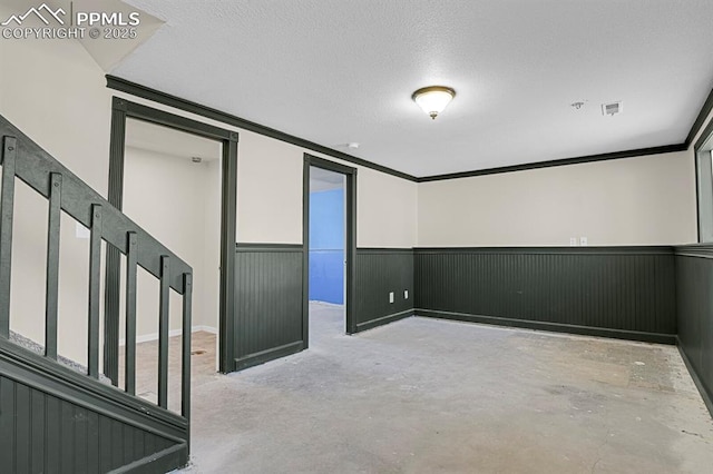 unfurnished room with a textured ceiling, concrete flooring, a wainscoted wall, visible vents, and ornamental molding