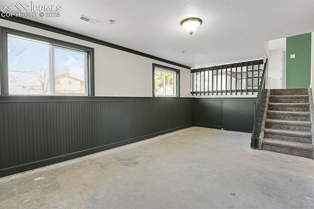 empty room with visible vents, a wainscoted wall, stairway, a textured ceiling, and concrete flooring