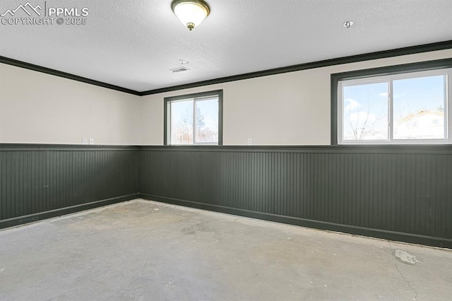 empty room featuring a textured ceiling, ornamental molding, unfinished concrete flooring, and wainscoting