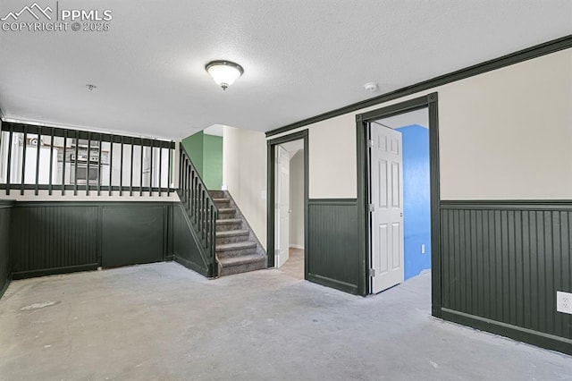 below grade area with wainscoting, stairway, and a textured ceiling