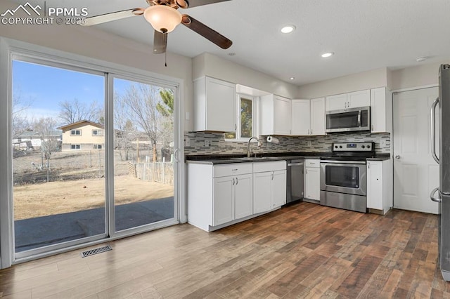 kitchen featuring a sink, visible vents, appliances with stainless steel finishes, backsplash, and dark countertops