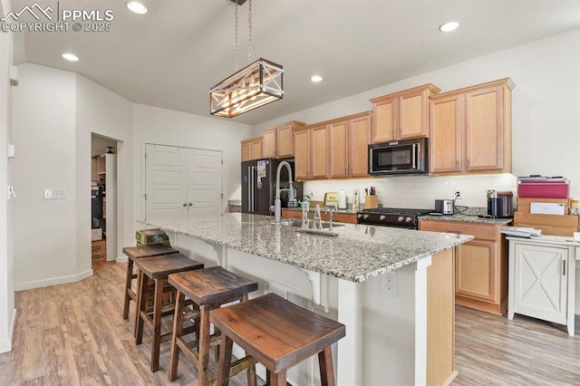 kitchen with a center island with sink, tasteful backsplash, recessed lighting, light wood-style flooring, and black appliances