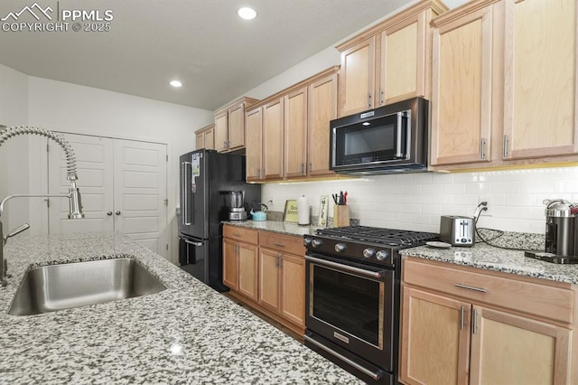 kitchen featuring light stone counters, recessed lighting, a sink, backsplash, and black appliances