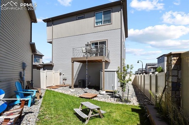 rear view of house featuring a fenced backyard, a yard, a balcony, and central air condition unit