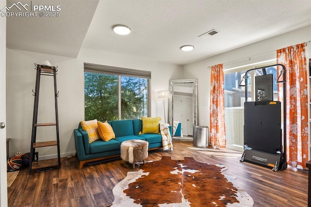 living room featuring baseboards, a textured ceiling, visible vents, and wood finished floors