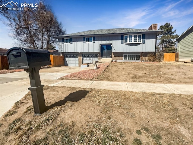 split foyer home with driveway, a garage, a chimney, fence, and board and batten siding