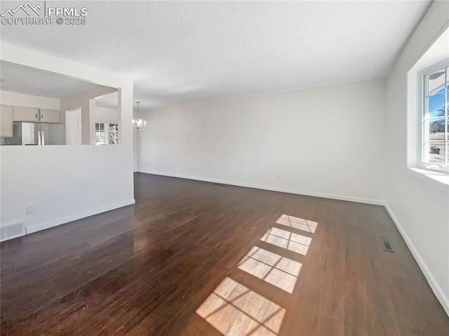 spare room featuring an inviting chandelier, a textured ceiling, visible vents, and dark wood-style flooring