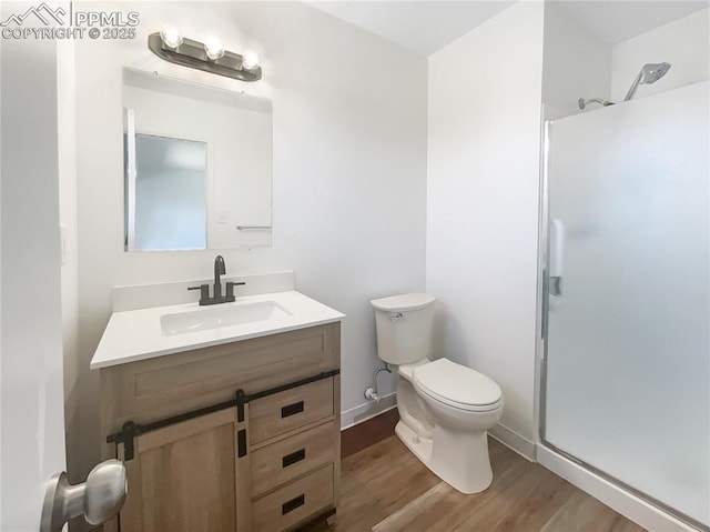 bathroom with a stall shower, vanity, toilet, and wood finished floors