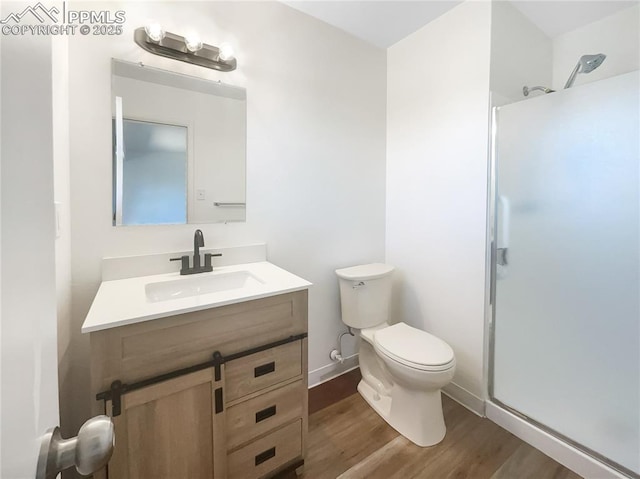 bathroom featuring toilet, wood finished floors, vanity, baseboards, and a stall shower