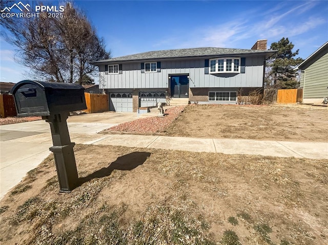 bi-level home featuring driveway, a chimney, fence, and board and batten siding